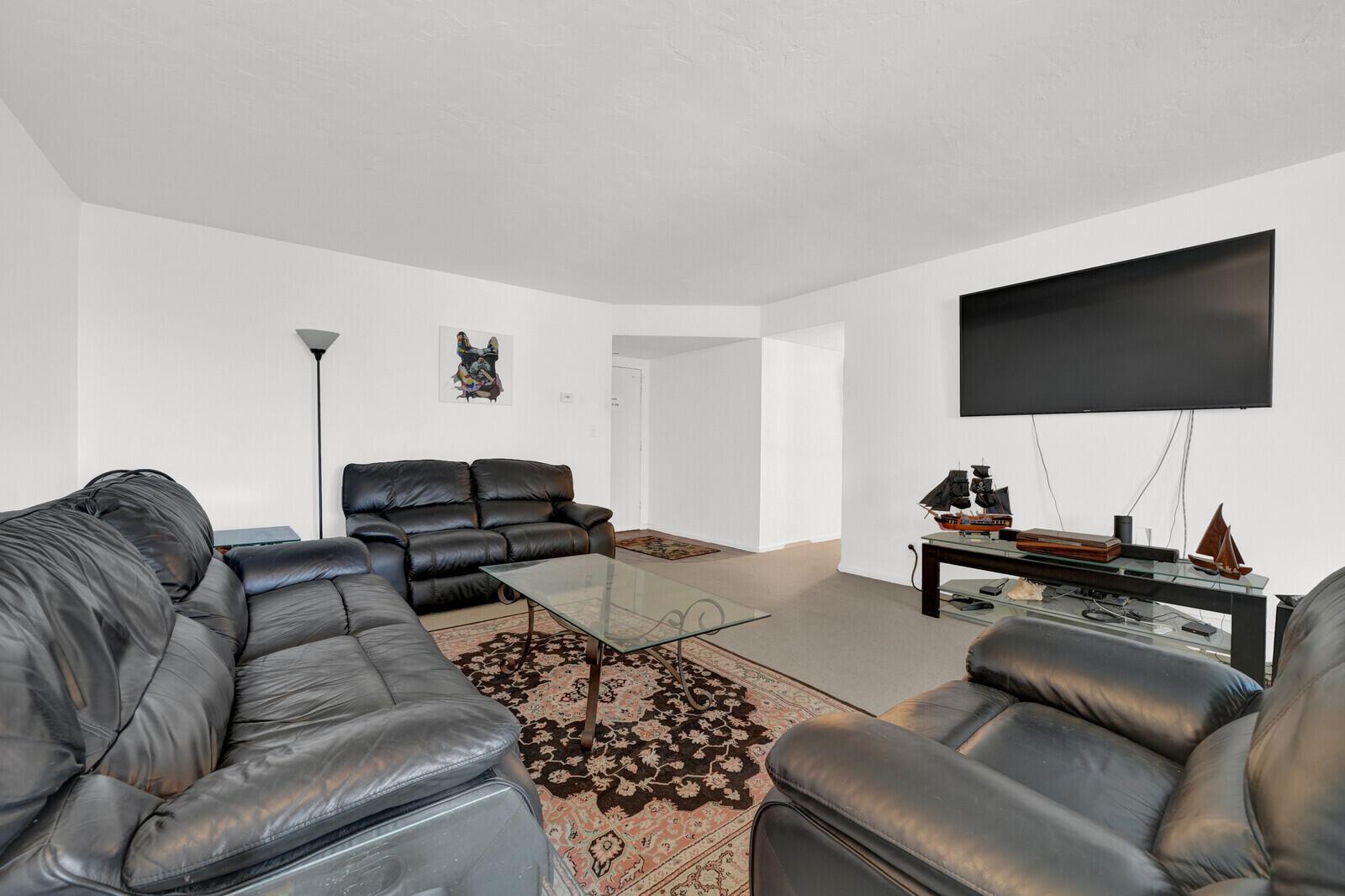 A living room features black leather sofas, a glass coffee table, and a wall-mounted television — 1000 S Ocean Boulevard # o, Pompano Beach FL 33062, POMPANO BEACH, FL