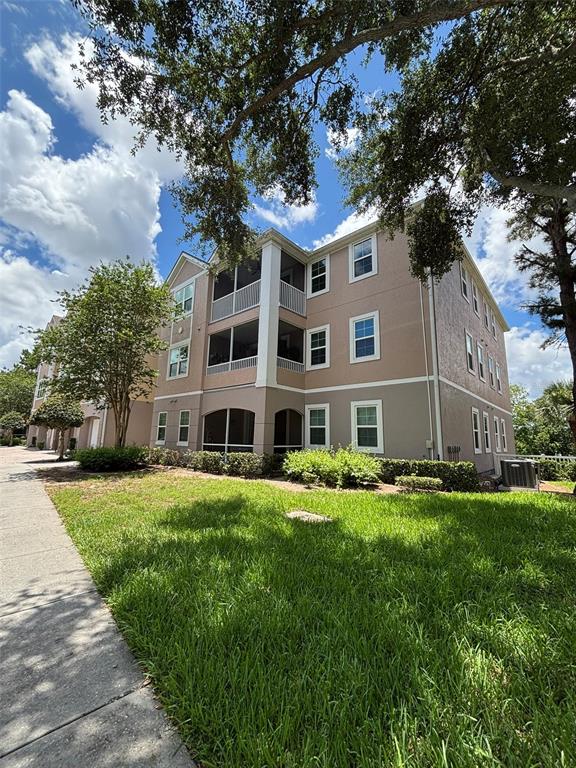 A three-story apartment building features tan stucco walls, screened balconies, and a grassy lawn — 3468 SOHO STREET UNIT 303, ORLANDO, FL