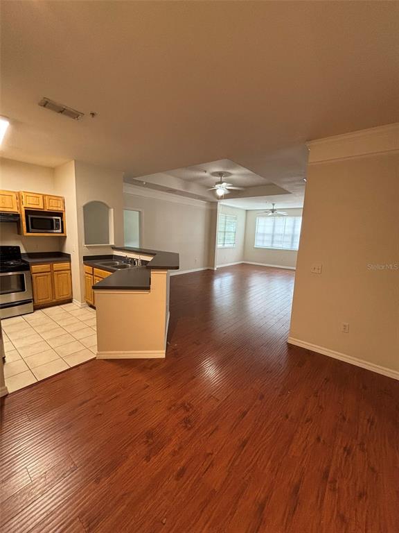 An open-concept kitchen with wood cabinets and tile floors transitions into a hardwood-floored living area — 3468 SOHO STREET UNIT 303, ORLANDO, FL