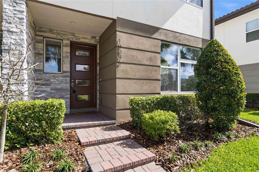A modern home entrance features a brown door, stone veneer siding, and a paved walkway — 10096 SUNNIFA ALLEY, ORLANDO, FL