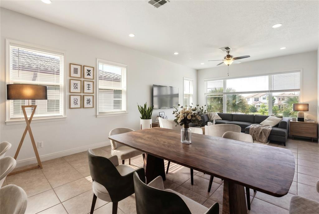 A dining room with a large wooden table, modern chairs, and an adjacent living area — 10096 SUNNIFA ALLEY, ORLANDO, FL