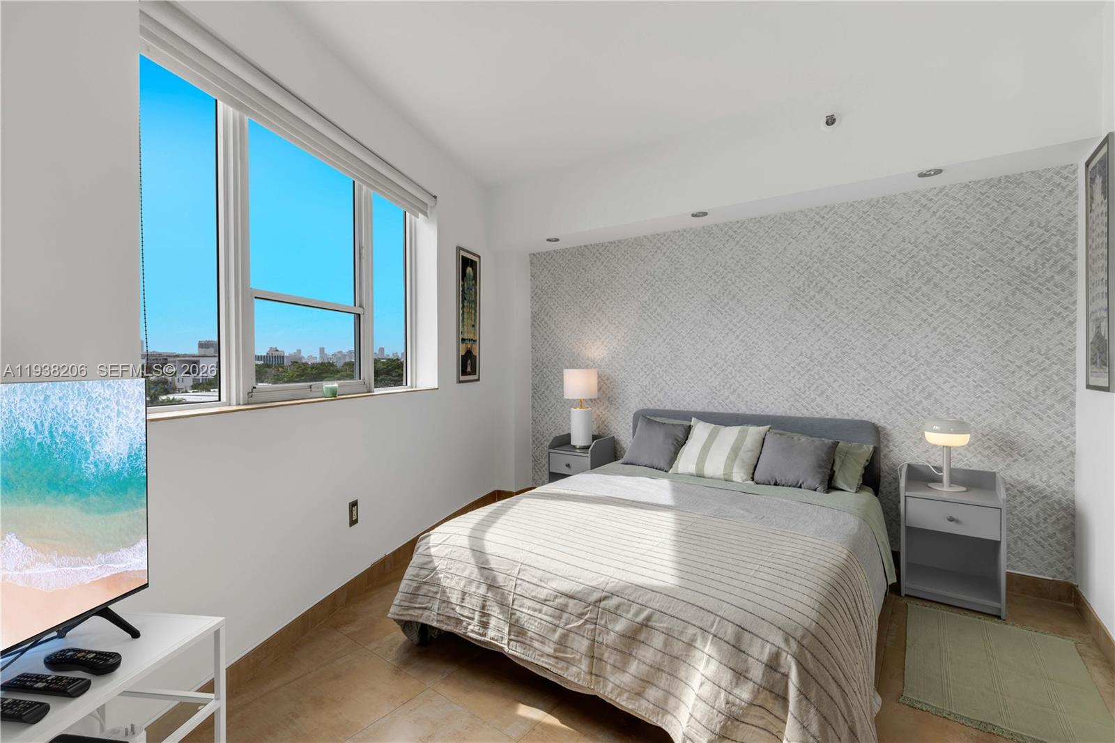 A bedroom features a bed with grey bedding, patterned wallpaper, and a window with city views — 255 W 24th St # 542, Miami Beach FL 33140, MIAMI BEACH, FL