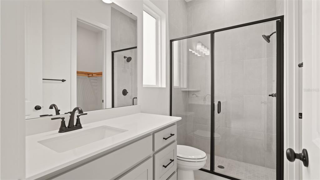 A bathroom features a white vanity with a black faucet, a toilet, and a glass shower — 5590 VIBRANT VINE DRIVE, WIMAUMA, FL