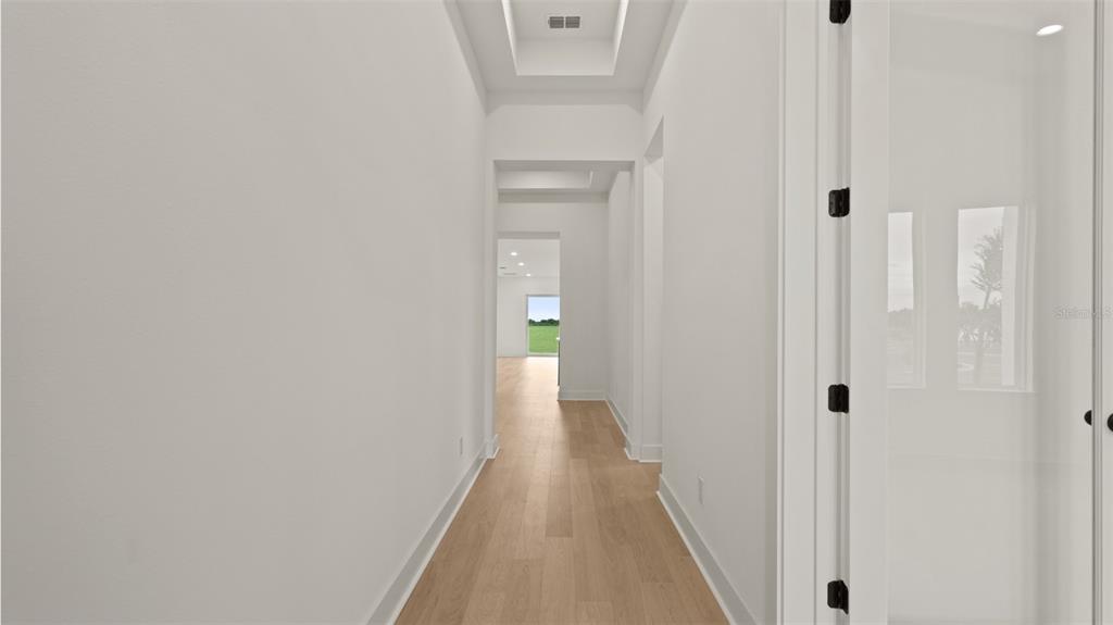 A bright hallway with light wood flooring leads toward an open living area with windows — 5590 VIBRANT VINE DRIVE, WIMAUMA, FL