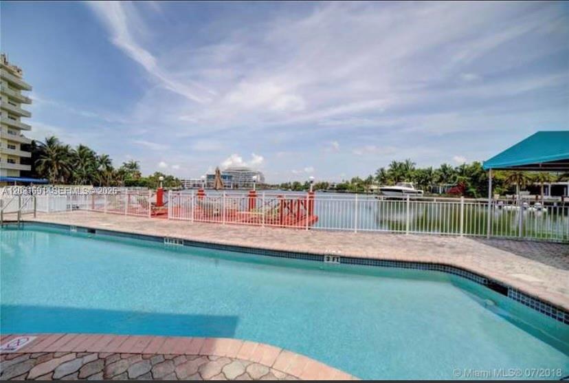 A swimming pool overlooks a canal with a white fence and a boat dock — 4740 Pine Tree Dr # 25, Miami Beach FL 33140, MIAMI BEACH, FL