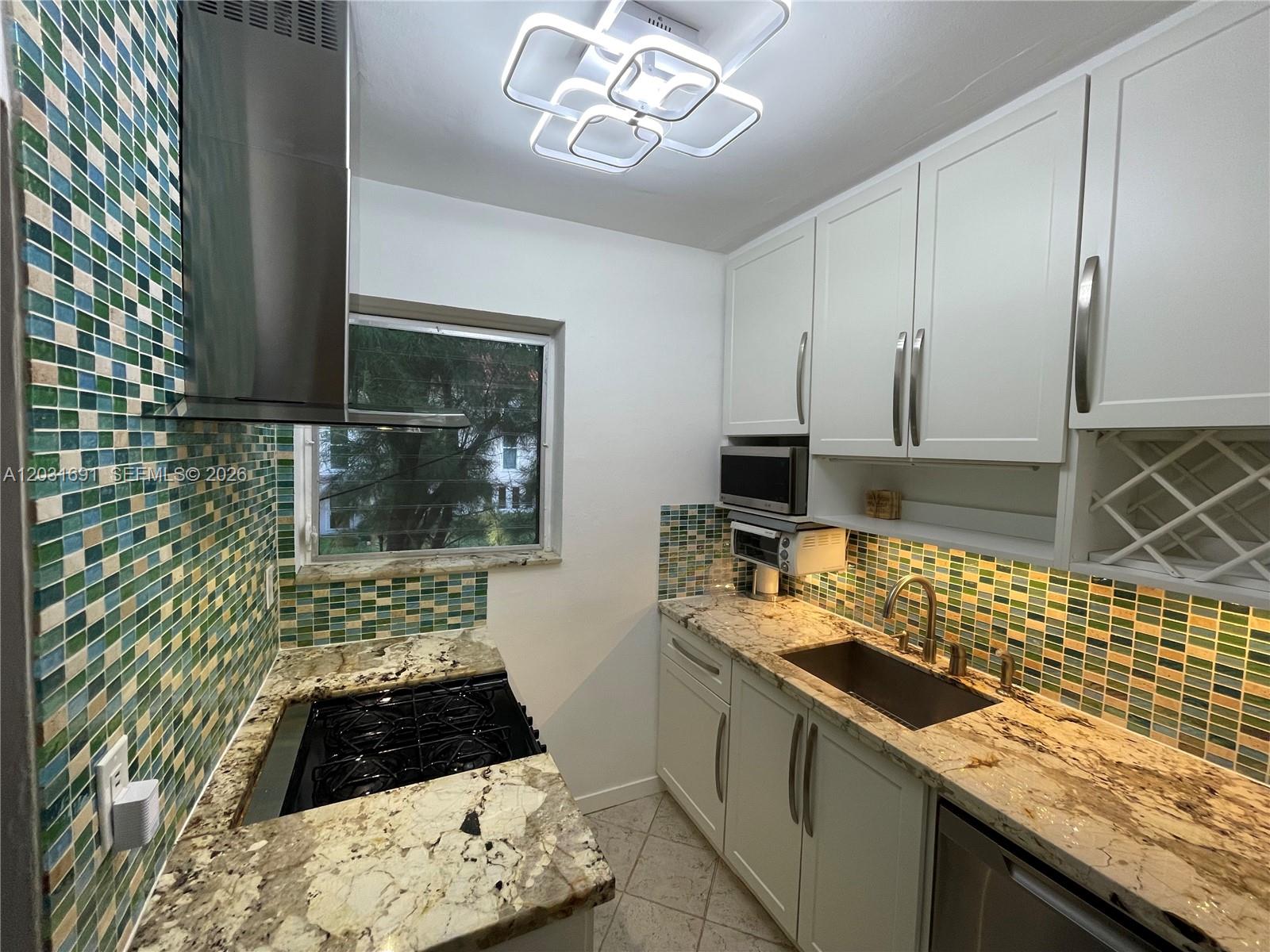 A kitchen features white cabinets, granite countertops, and a multi-colored mosaic tile backsplash — 4740 Pine Tree Dr # 25, Miami Beach FL 33140, MIAMI BEACH, FL