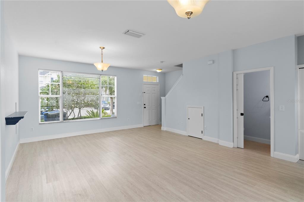 A bright, empty living room features light wood-look flooring, pale blue walls, and a window — 12294 COUNTRY WHITE CIRCLE, TAMPA, FL