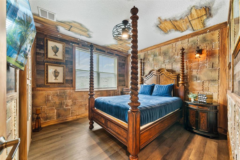 A bedroom features a four-poster bed, stone-textured walls, wood paneling, and damaged ceiling sections — 1187 KINGSBARN STREET, DAVENPORT, FL