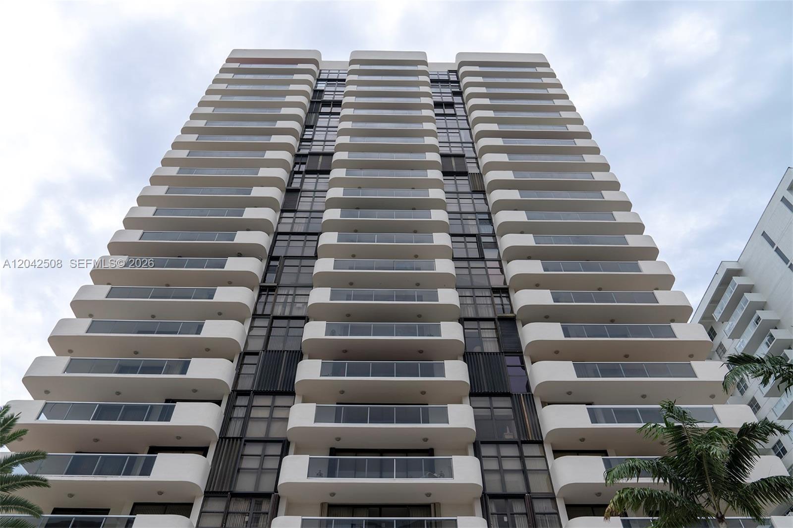 A low-angle view of a tall residential building featuring stacked balconies and glass windows — 5757 Collins Ave # 1604, Miami Beach FL 33140, MIAMI BEACH, FL