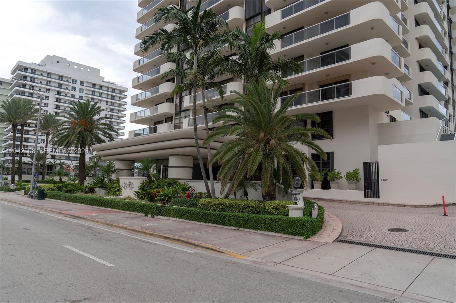 A multi-story white residential building features balconies, palm trees, and a paved driveway entrance — 5757 Collins Ave # 1604, Miami Beach FL 33140, MIAMI BEACH, FL
