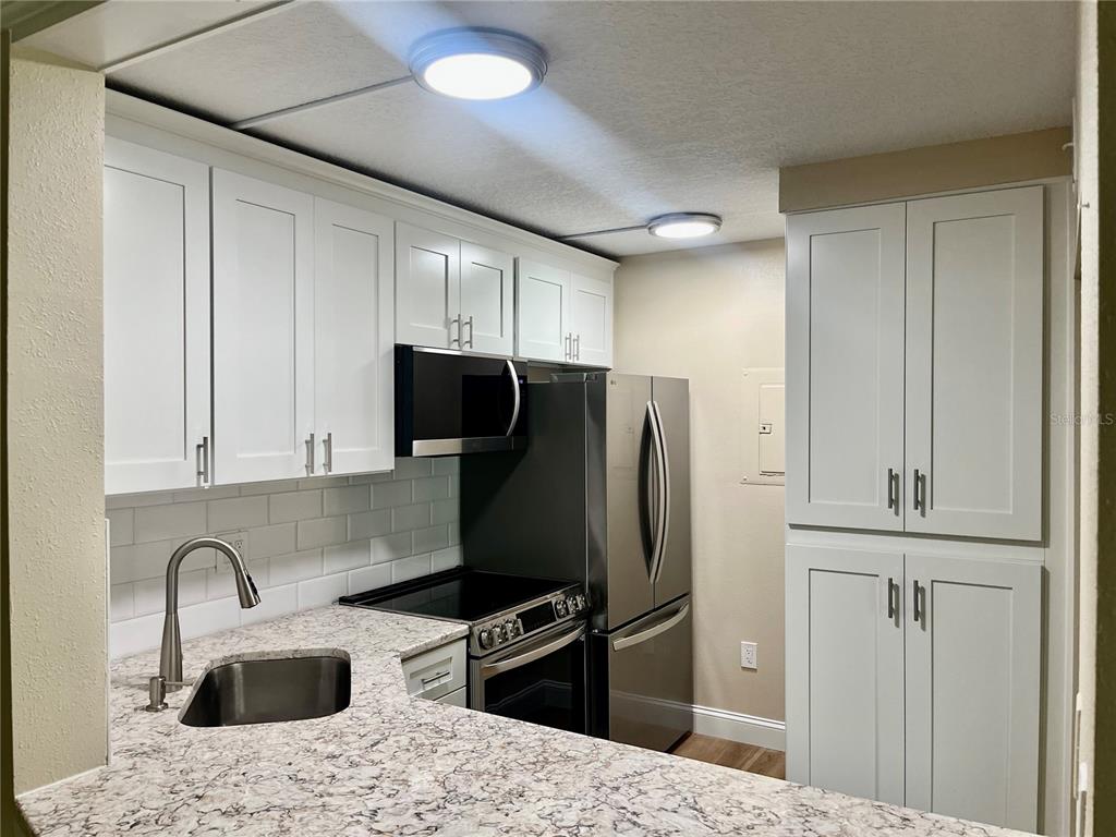 A kitchen features white shaker cabinets, granite countertops, stainless steel appliances, and a subway tile backsplash — 1423 PINE GLEN LANE UNIT H2, TARPON SPRINGS, FL