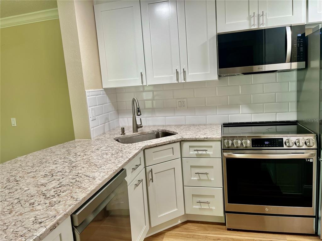 A kitchen with white cabinets, stainless steel appliances, subway tile backsplash, and patterned countertops — 1423 PINE GLEN LANE UNIT H2, TARPON SPRINGS, FL