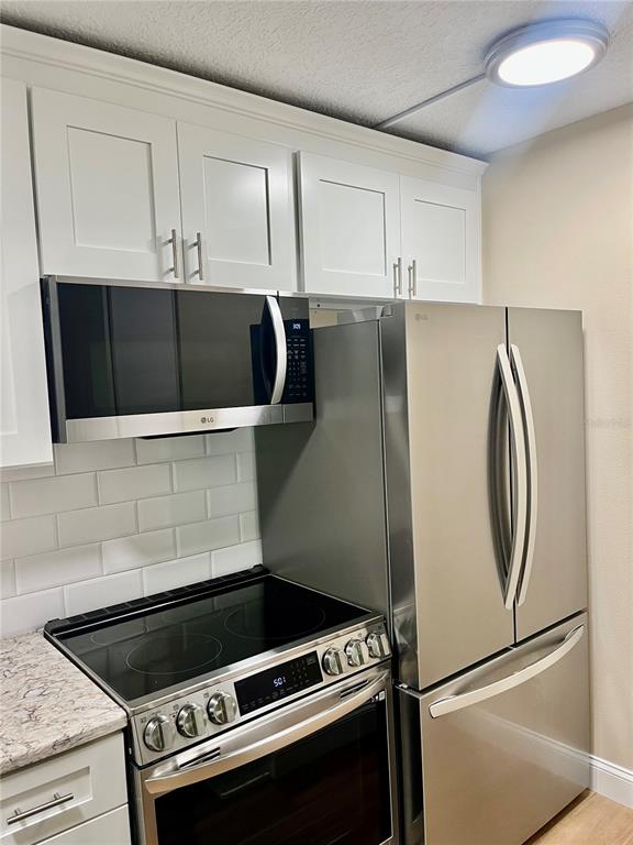 A kitchen features white cabinets, stainless steel appliances, and a subway tile backsplash — 1423 PINE GLEN LANE UNIT H2, TARPON SPRINGS, FL