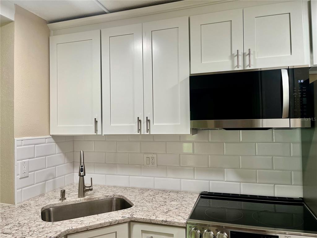 A kitchen featuring white shaker cabinets, a stainless steel microwave, and a subway tile backsplash — 1423 PINE GLEN LANE UNIT H2, TARPON SPRINGS, FL