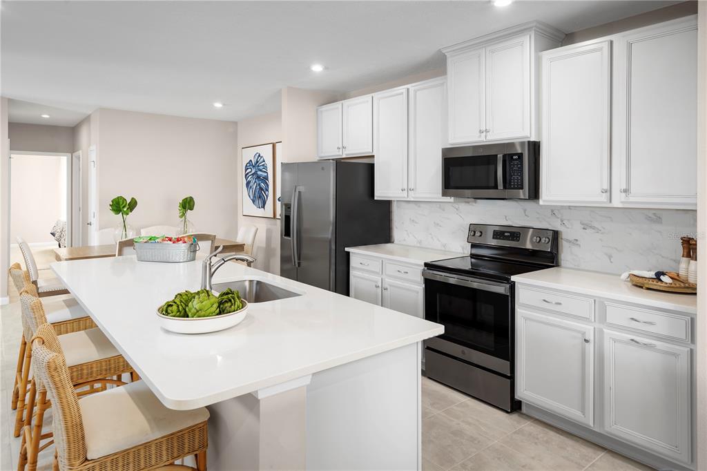 A modern kitchen features white cabinets, stainless steel appliances, and a large central island — 384 BALI STREET, LADY LAKE, FL