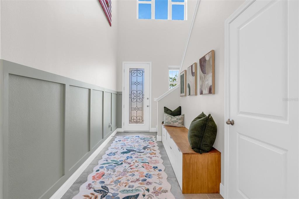 A bright entryway features a floral runner, a wooden bench, and gray wainscoting on the wall — 2019 SUNSHINE PEAK DRIVE, MINNEOLA, FL