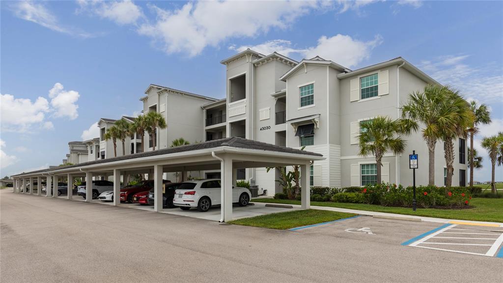 A multi-story apartment building features a covered parking structure with several parked cars — 43030 GREENWAY BOULEVARD UNIT 435, PUNTA GORDA, FL
