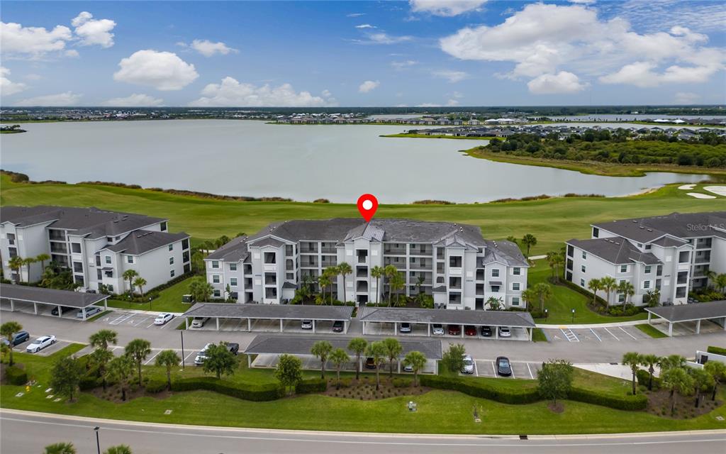 An aerial view of a multi-story apartment building with covered parking next to a lake — 43030 GREENWAY BOULEVARD UNIT 435, PUNTA GORDA, FL