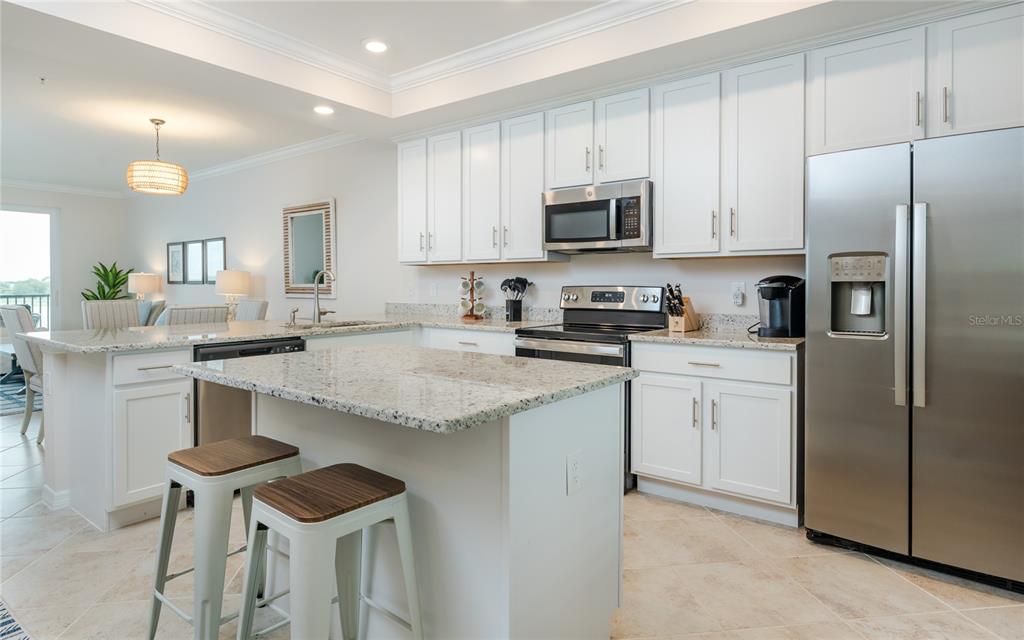 A modern kitchen features white cabinets, granite countertops, stainless steel appliances, and a central island — 43030 GREENWAY BOULEVARD UNIT 435, PUNTA GORDA, FL