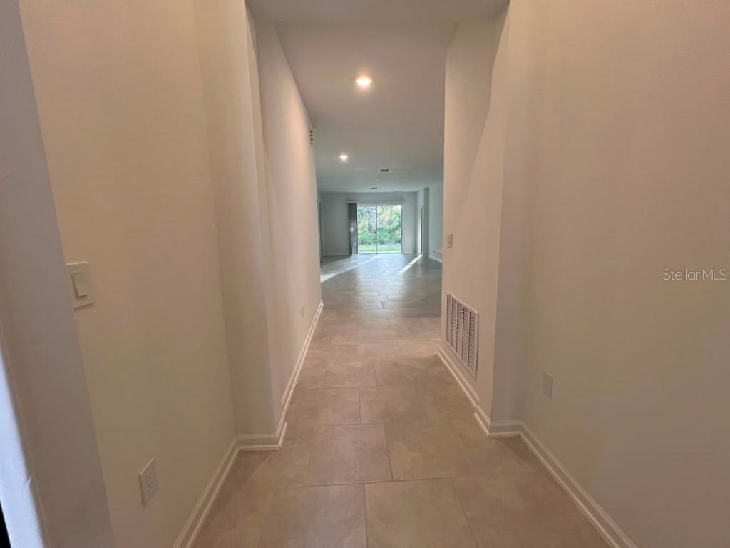A hallway with light-colored tile flooring leads toward a living area with sliding glass doors — 1378 PEACH CREEK DRIVE, OSTEEN, FL