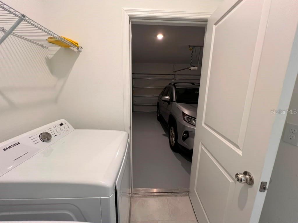 A laundry room with a white washer leads into a garage containing a silver car — 1378 PEACH CREEK DRIVE, OSTEEN, FL