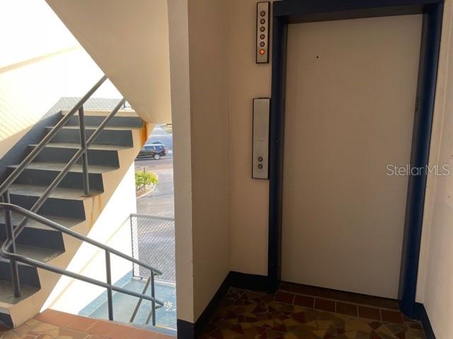 An indoor stairwell with metal railings sits next to an elevator with a control panel — 200 N BETTY LANE UNIT 3E, CLEARWATER, FL
