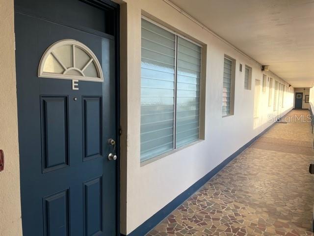 A dark blue door with a semi-circular window sits along an outdoor apartment building walkway — 200 N BETTY LANE UNIT 3E, CLEARWATER, FL