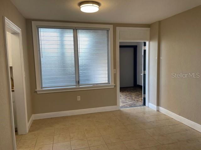 A room with beige walls, tile flooring, a window with blinds, and two doorways — 200 N BETTY LANE UNIT 3E, CLEARWATER, FL