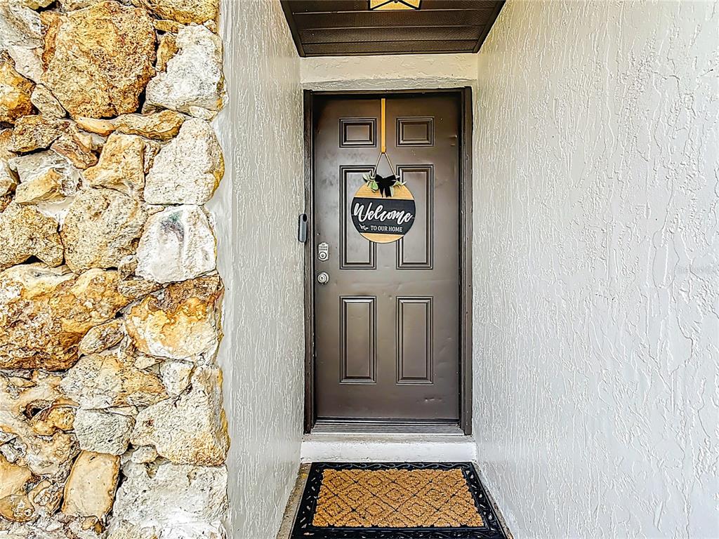 A dark brown front door with a welcome sign sits between a stone wall and white stucco — 2661 AMES HAVEN ROAD, KISSIMMEE, FL