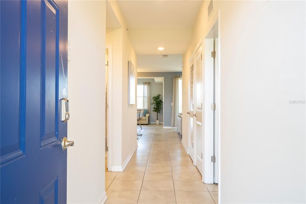 A tiled hallway leads from a blue front door toward a bright, open living area — 4731 CLOCK TOWER DRIVE UNIT 306, KISSIMMEE, FL