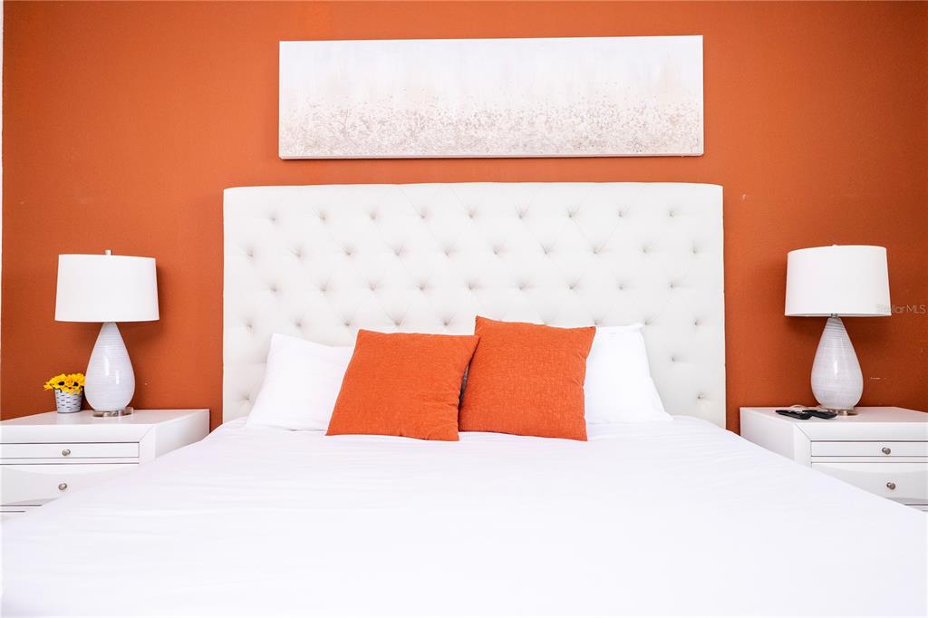 A bedroom features a white tufted headboard against an orange wall with matching bedside lamps — 4731 CLOCK TOWER DRIVE UNIT 306, KISSIMMEE, FL