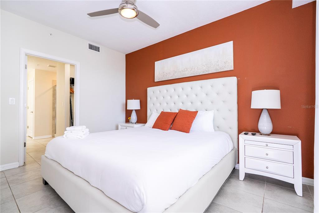 A bedroom features a white tufted headboard, white bedding, and an accent wall painted orange — 4731 CLOCK TOWER DRIVE UNIT 306, KISSIMMEE, FL