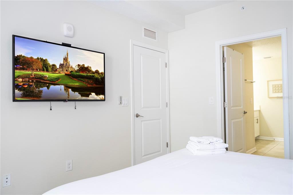 A bedroom features a wall-mounted television, a white door, and an open doorway to a bathroom — 4731 CLOCK TOWER DRIVE UNIT 306, KISSIMMEE, FL