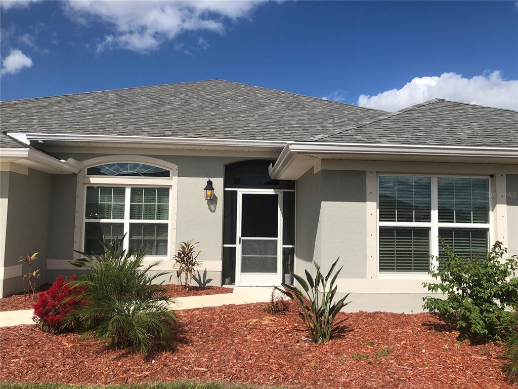 A single-story house with a gray stucco exterior, a shingled roof, and a screened entryway — 26332 BARRANQUILLA AVENUE, PUNTA GORDA, FL