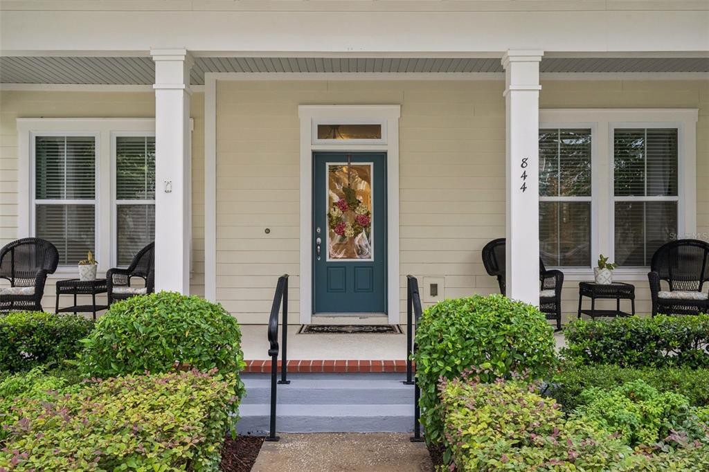 A front porch with a teal door, white columns, and wicker chairs sits behind bushes — 844 OAKLAND PARK BOULEVARD, WINTER GARDEN, FL
