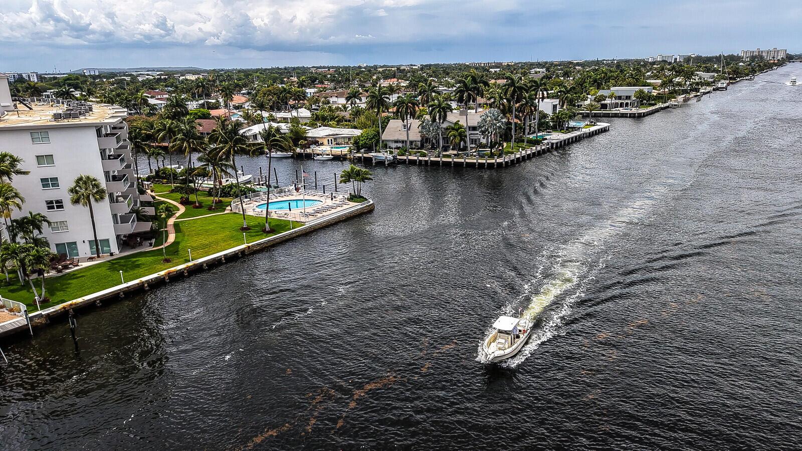 An aerial view shows a boat traveling down a canal past waterfront homes and apartments — 140 NE 28th Avenue # 502, Pompano Beach FL 33062, POMPANO BEACH, FL