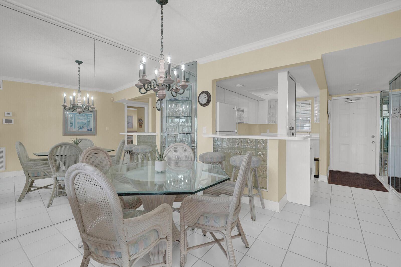 A dining area with a glass table, wicker chairs, a chandelier, and a mirrored wall — 140 NE 28th Avenue # 502, Pompano Beach FL 33062, POMPANO BEACH, FL