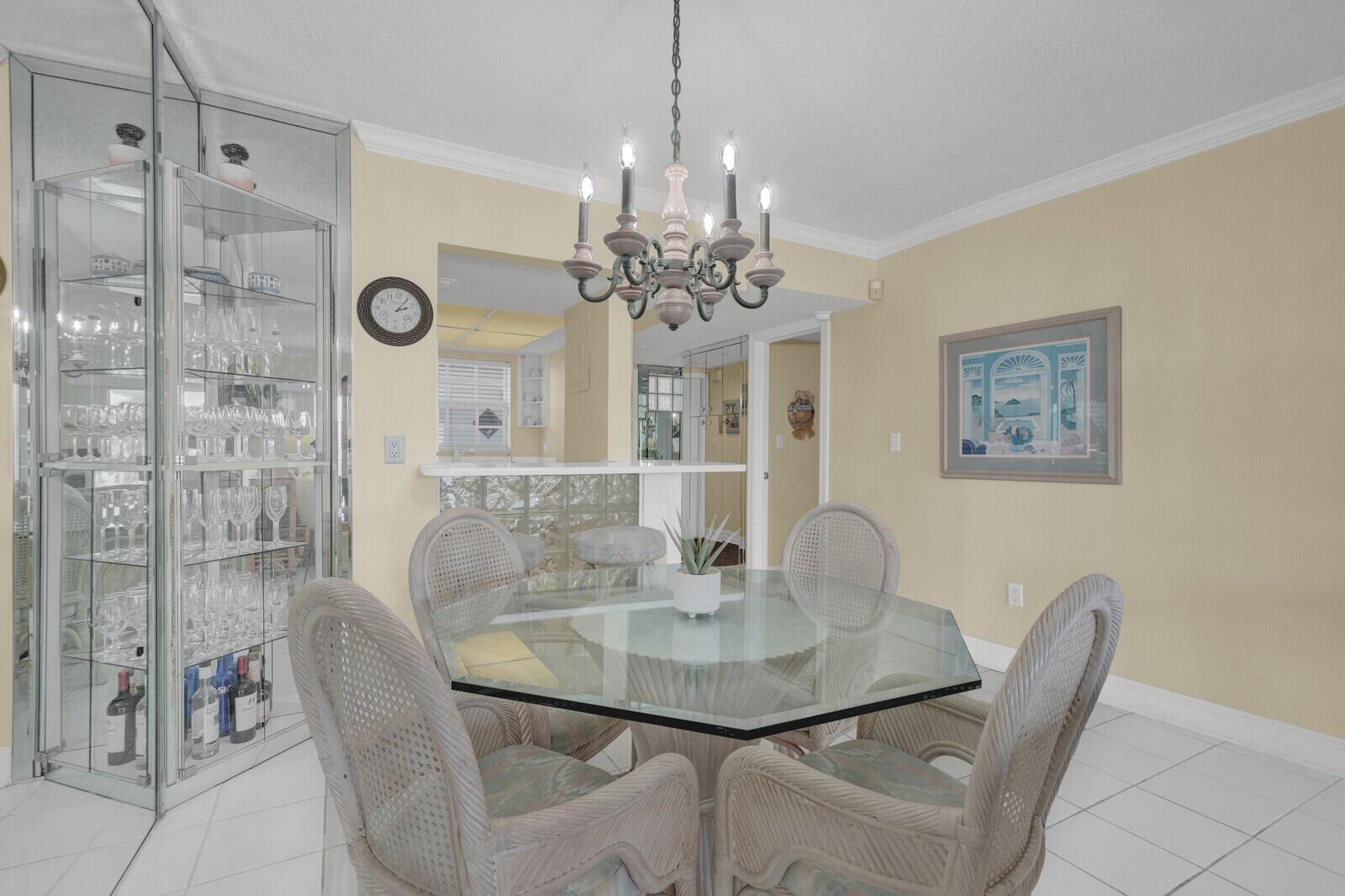 A dining area features a glass-topped table, wicker chairs, a chandelier, and a mirrored cabinet — 140 NE 28th Avenue # 502, Pompano Beach FL 33062, POMPANO BEACH, FL
