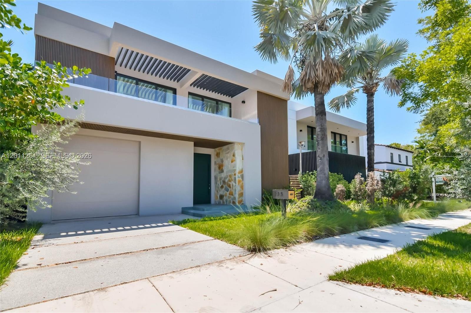 A modern two-story house features a concrete driveway, stone accents, and a glass-railed balcony — 135 SW 29th Rd, Miami FL 33129, MIAMI, FL