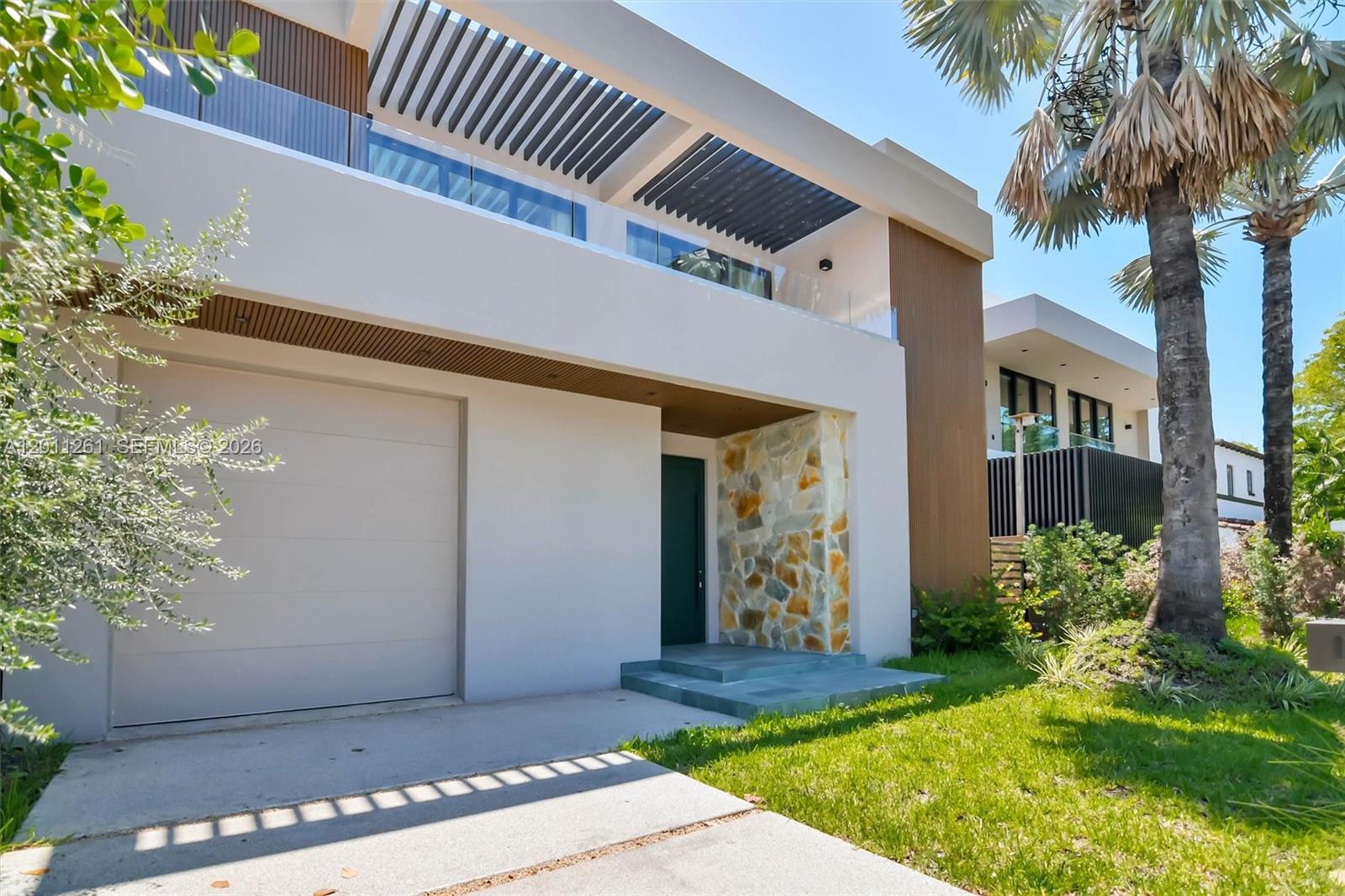 A modern two-story house features a garage, stone accent wall, and a slatted roof balcony — 135 SW 29th Rd, Miami FL 33129, MIAMI, FL