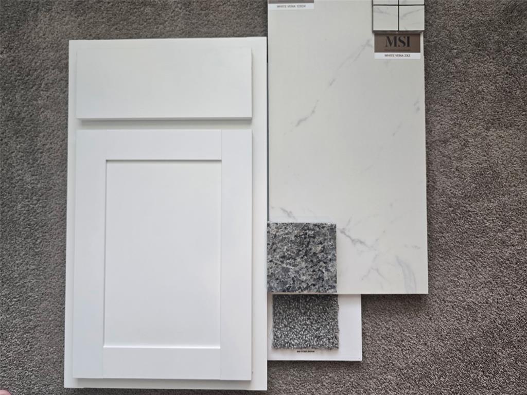 A white shaker cabinet door sits next to a marble-look tile sample and carpet swatches — 8 DIANTHUS COURT, HOMOSASSA, FL