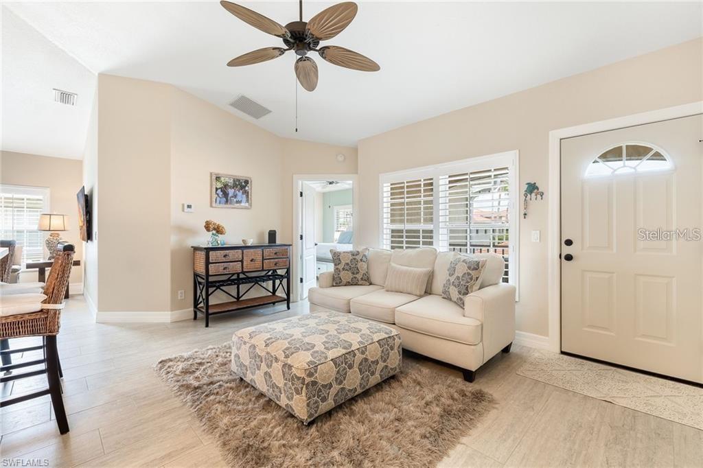 A living room features a white sofa, patterned ottoman, ceiling fan, and tile flooring — 10202 L PAVIA BOULEVARD UNIT 10202, VENICE, FL