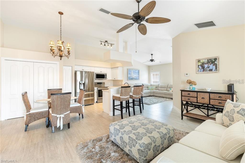 An open-concept living and dining area features light tile flooring, wicker furniture, and neutral walls — 10202 L PAVIA BOULEVARD UNIT 10202, VENICE, FL