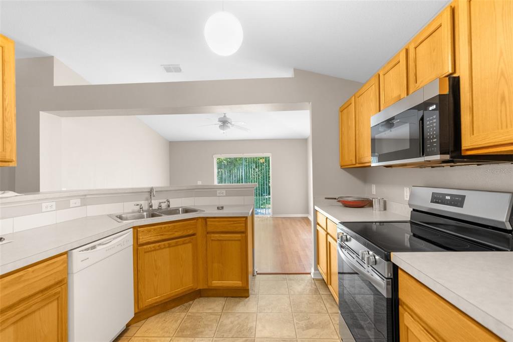 A kitchen with wood cabinets, stainless steel appliances, and tile flooring overlooks a living area — 3220 BELLERICAY LANE, LAND O LAKES, FL