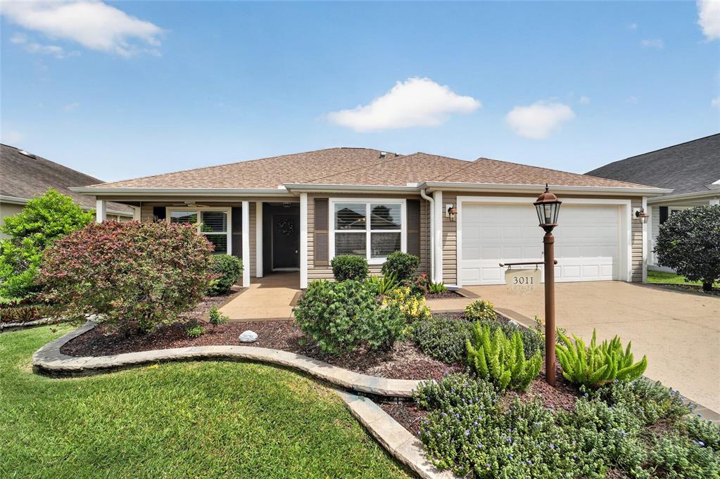 A single-story house with a tan exterior, a two-car garage, and a landscaped front yard — 3011 SPANISH MOSS WAY, THE VILLAGES, FL