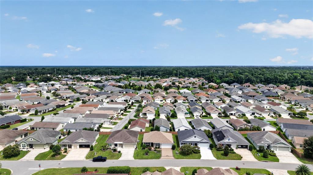 An aerial view shows a suburban neighborhood with many single-story houses and paved streets — 3011 SPANISH MOSS WAY, THE VILLAGES, FL