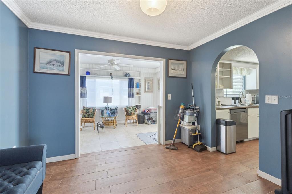 A blue-walled living room features wood-look tile flooring, an arched kitchen entrance, and a sunroom — 17841 SE 106TH COURT, SUMMERFIELD, FL