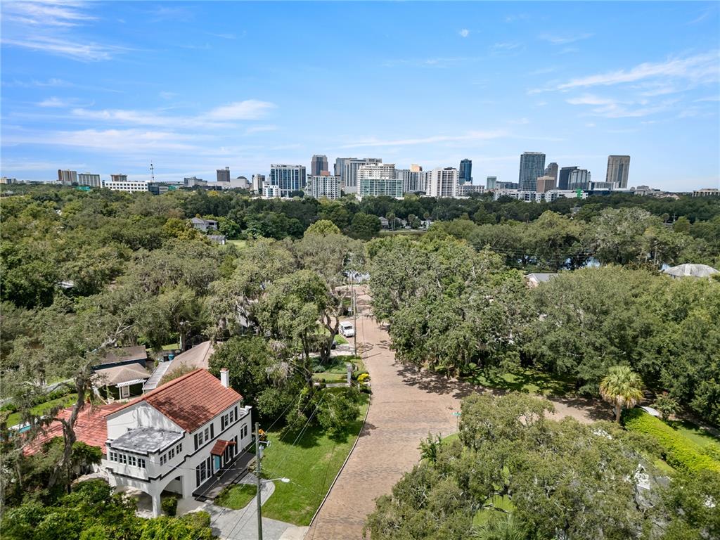 An aerial view shows a residential street with a house and trees facing a city skyline — 1408 E CHURCH STREET, ORLANDO, FL