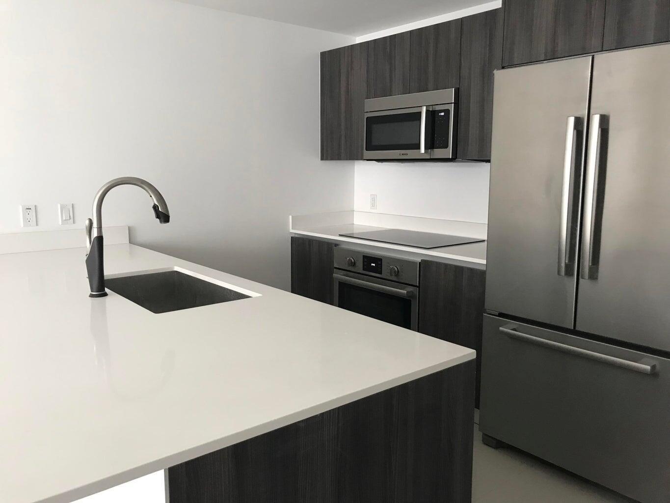 A modern kitchen features dark wood cabinetry, stainless steel appliances, and a white quartz island — 488 NE 18th Street # 807, Miami FL 33132, MIAMI, FL