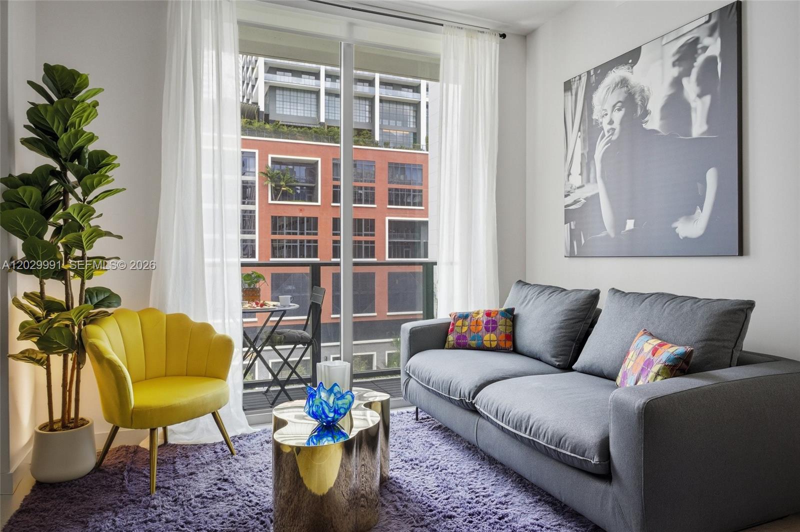 A living room features a grey sofa, yellow chair, purple rug, and a balcony view — 121 NE 5th St # 711, Miami FL 33132, MIAMI, FL